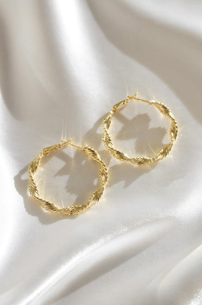 Gold hoop earrings on a white fabric background