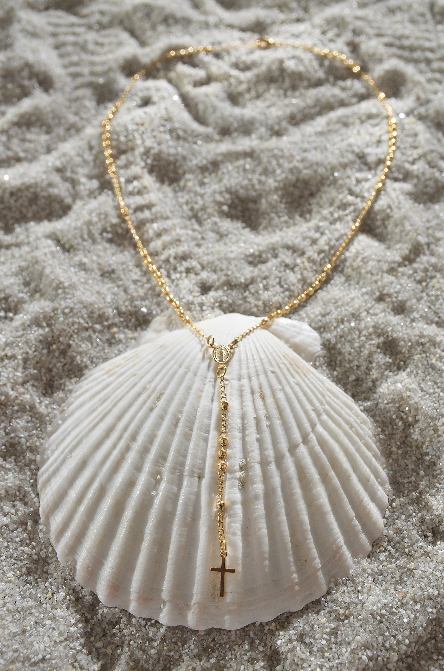 A 18K Gold Filled Dainty Rosary Necklace on a seashell. By DBL Jewelry