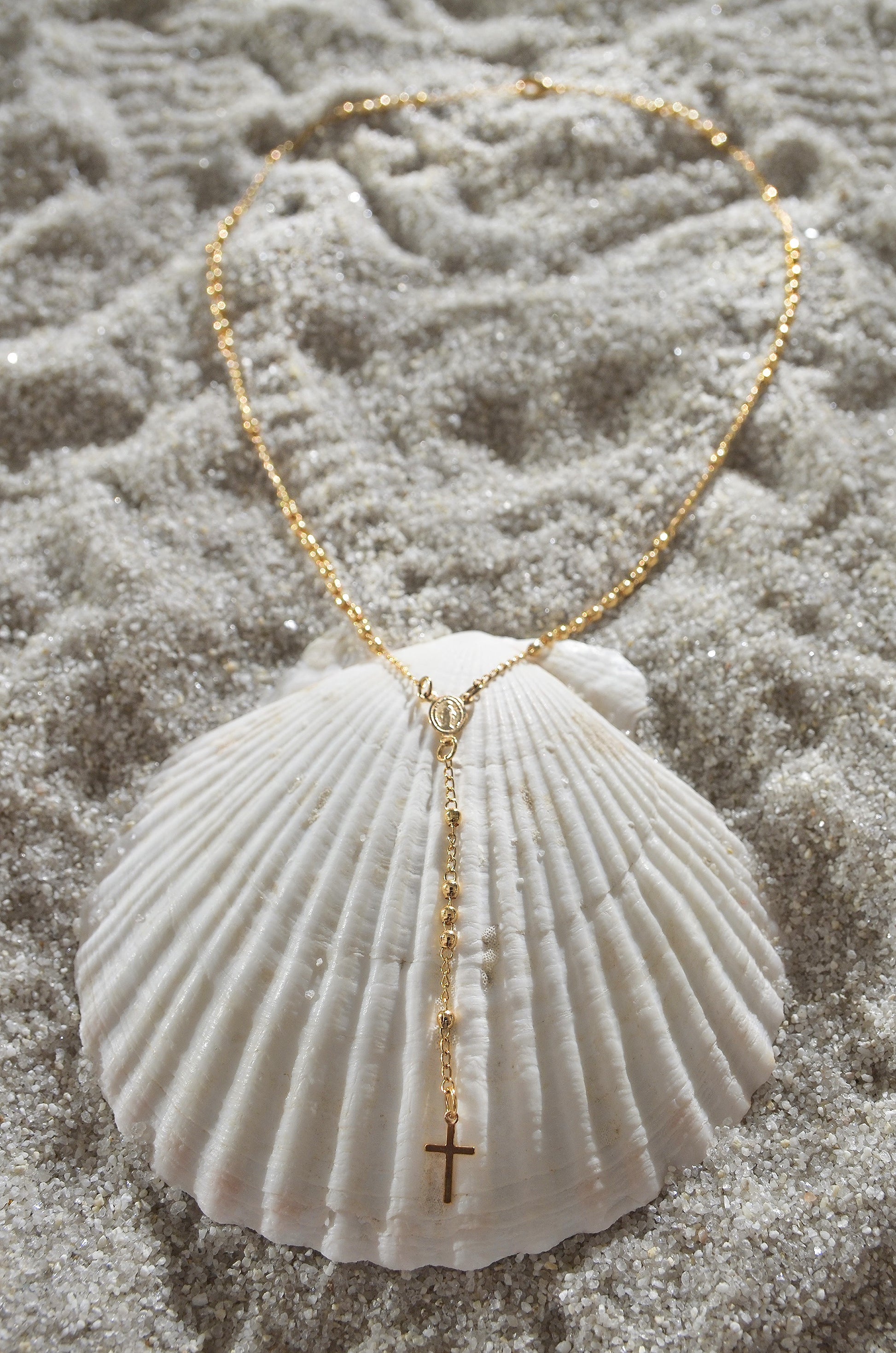 A 18K Gold Filled Dainty Rosary Necklace on a seashell. By DBL Jewelry