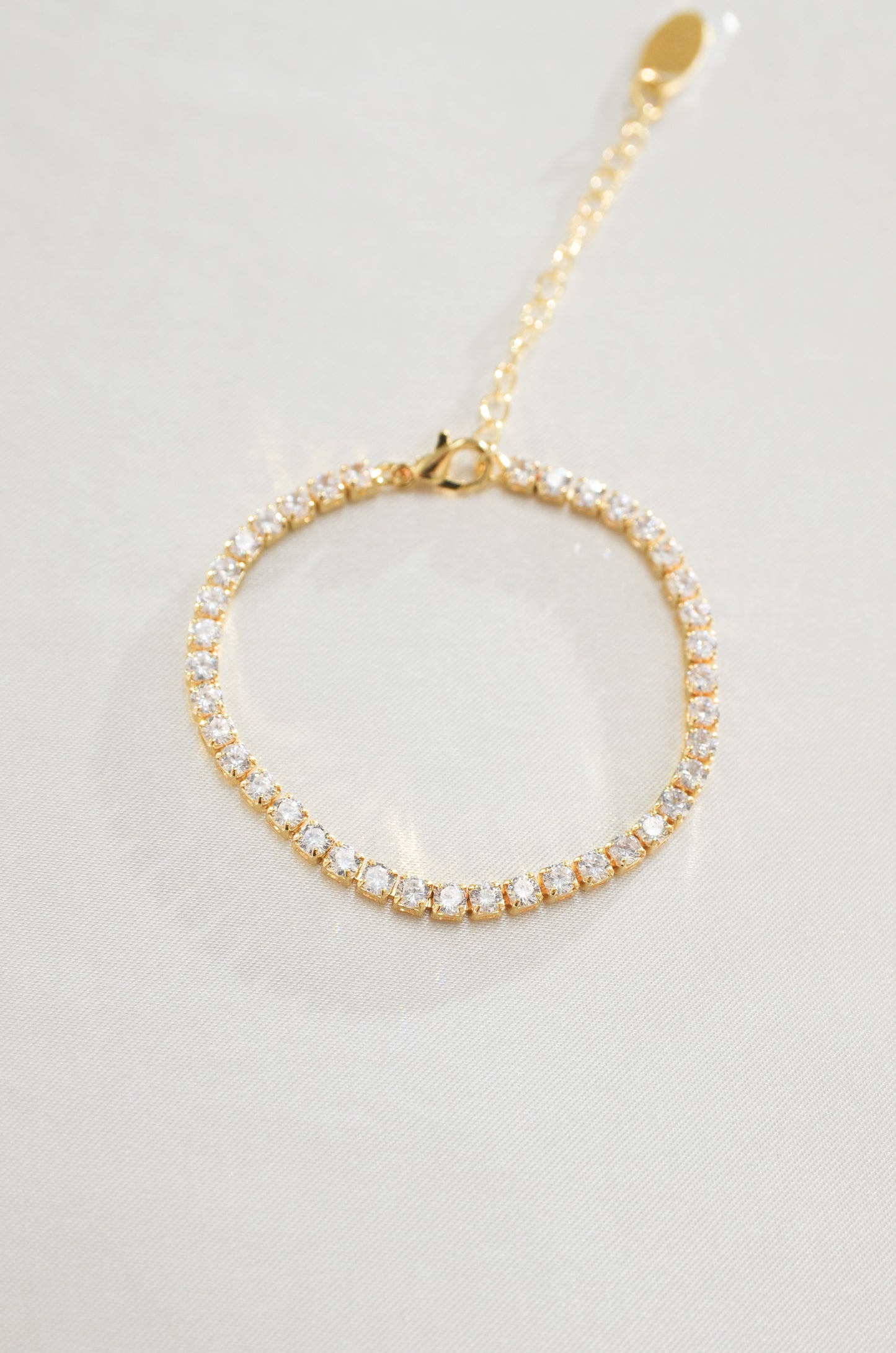 A gold-filled tennis bracelet surrounded by cubic zirconia diamond stones, displayed against a white background. By DBL Jewelry