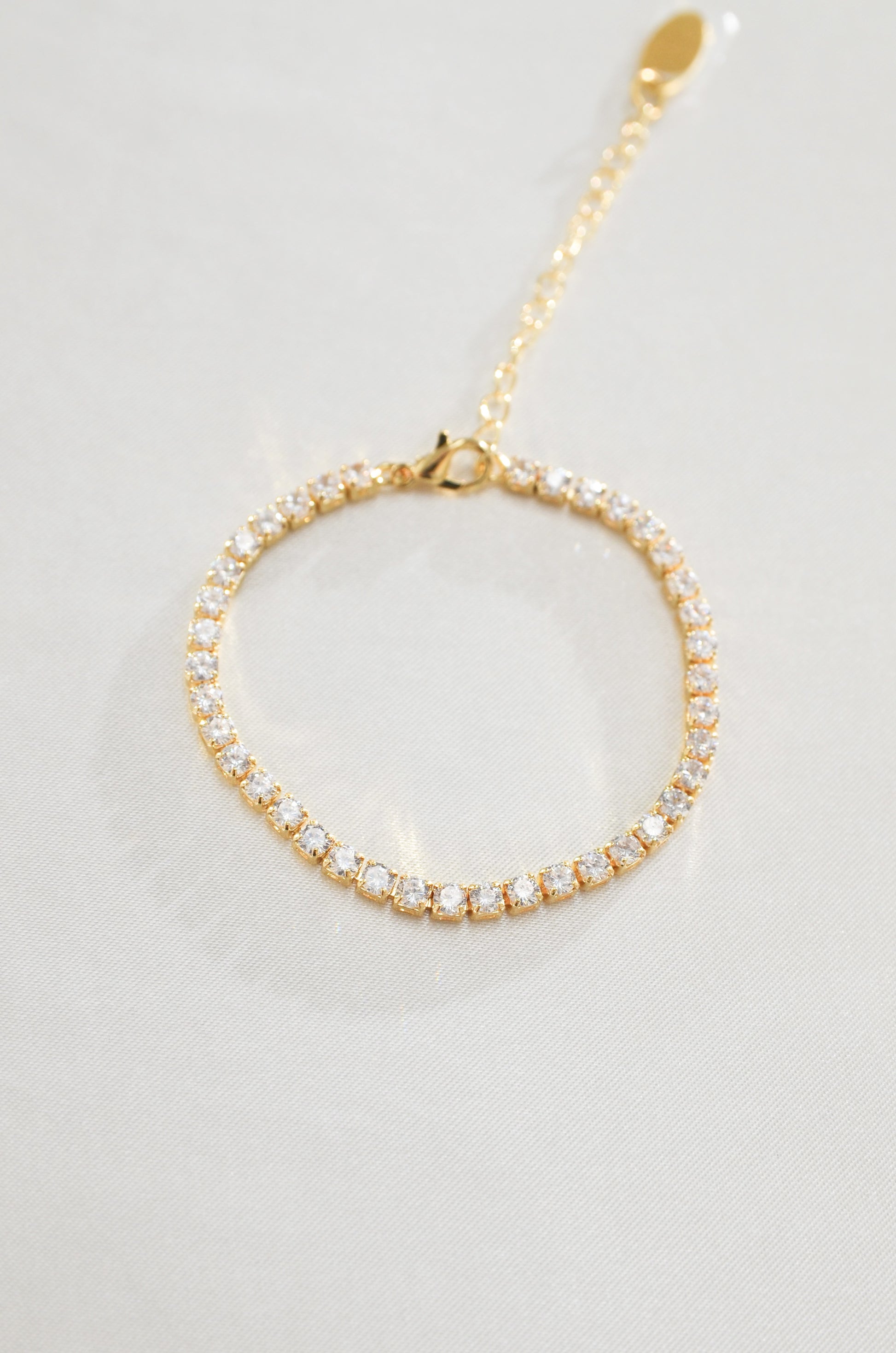 A gold-filled tennis bracelet surrounded by cubic zirconia diamond stones, displayed against a white background. By DBL Jewelry