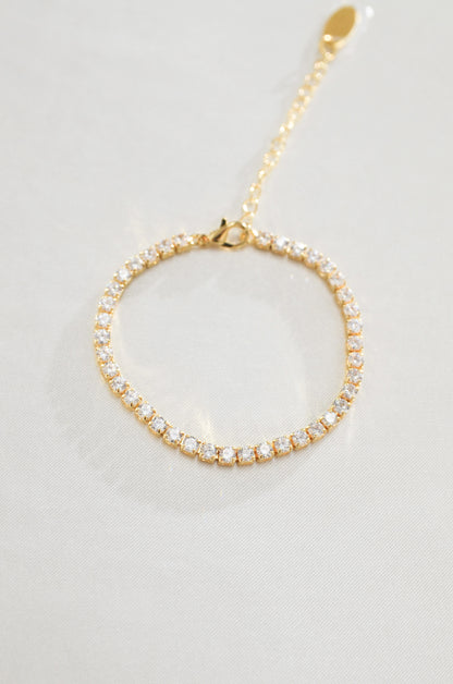 A gold-filled tennis bracelet surrounded by cubic zirconia diamond stones, displayed against a white background. By DBL Jewelry