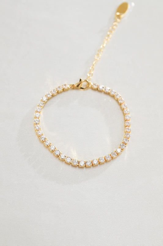 A gold-filled tennis bracelet surrounded by cubic zirconia diamond stones, displayed against a white background. By DBL Jewelry