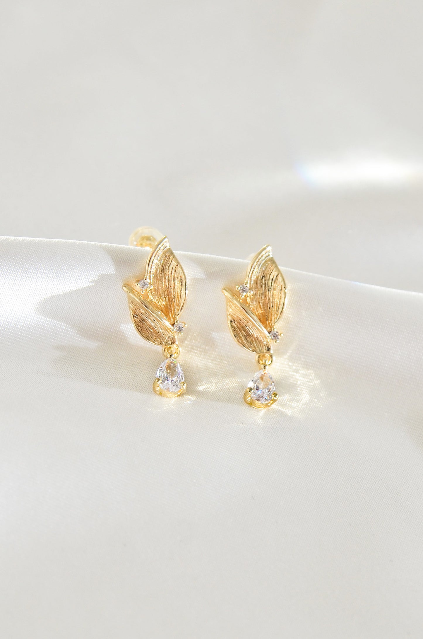 A pair of gold-filled leaf-shaped earrings with a fairy motif, featuring small clear stones at the bottom. By DBL Jewelry
