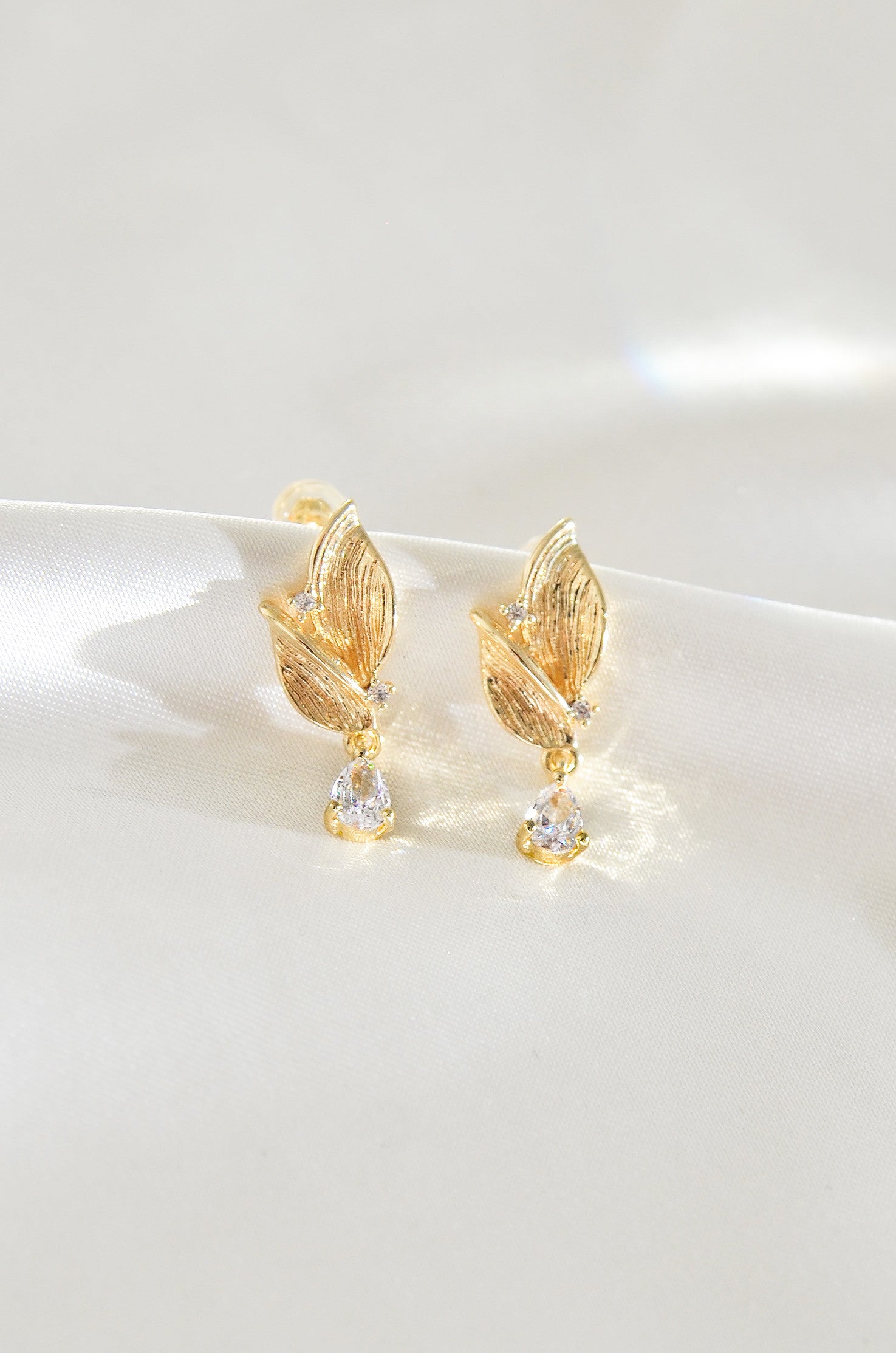 A pair of gold-filled leaf-shaped earrings with a fairy motif, featuring small clear stones at the bottom. By DBL Jewelry