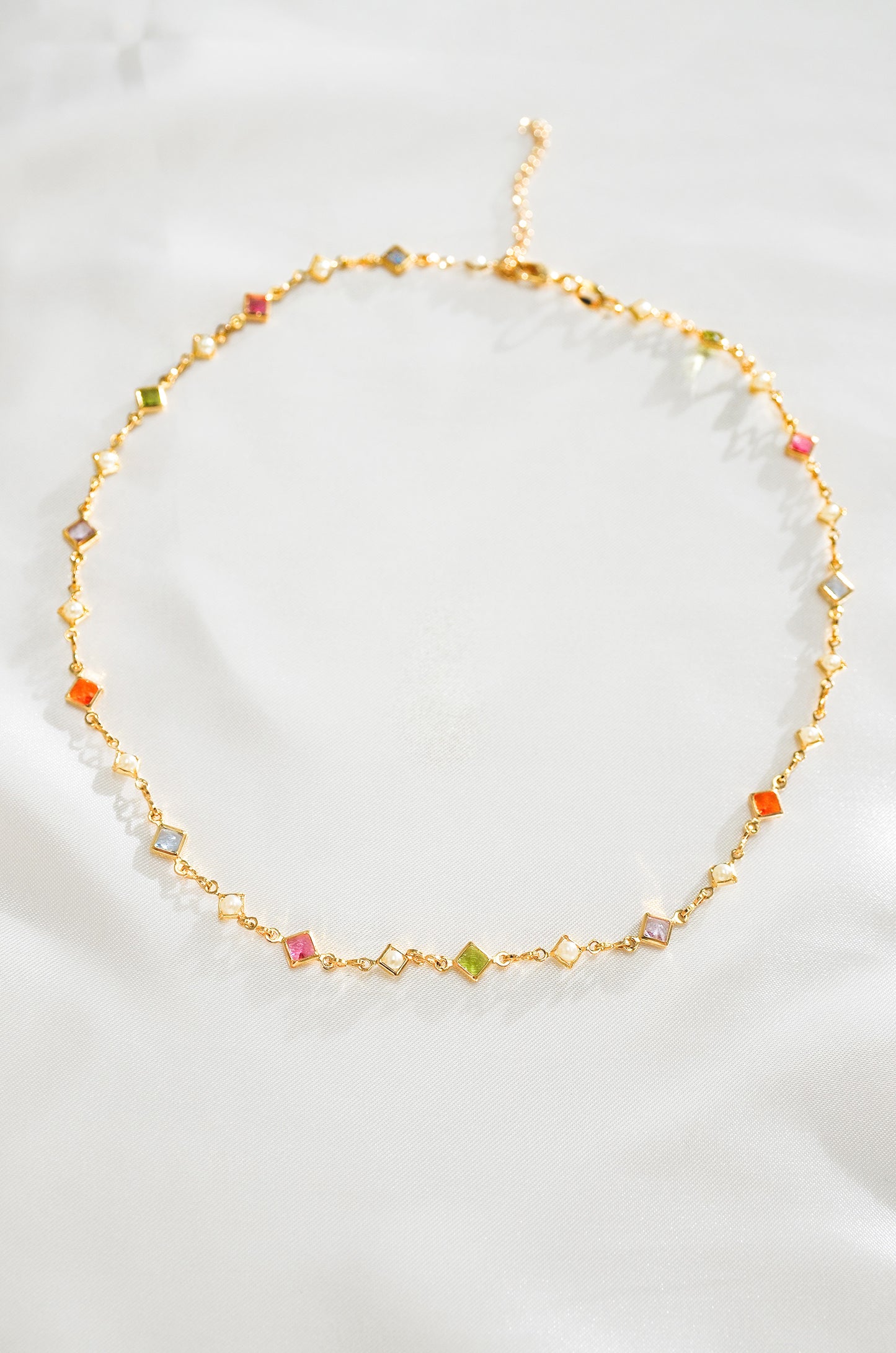 A gold-colored necklace with a series of multicolored crystal beads arranged in a chain link pattern.