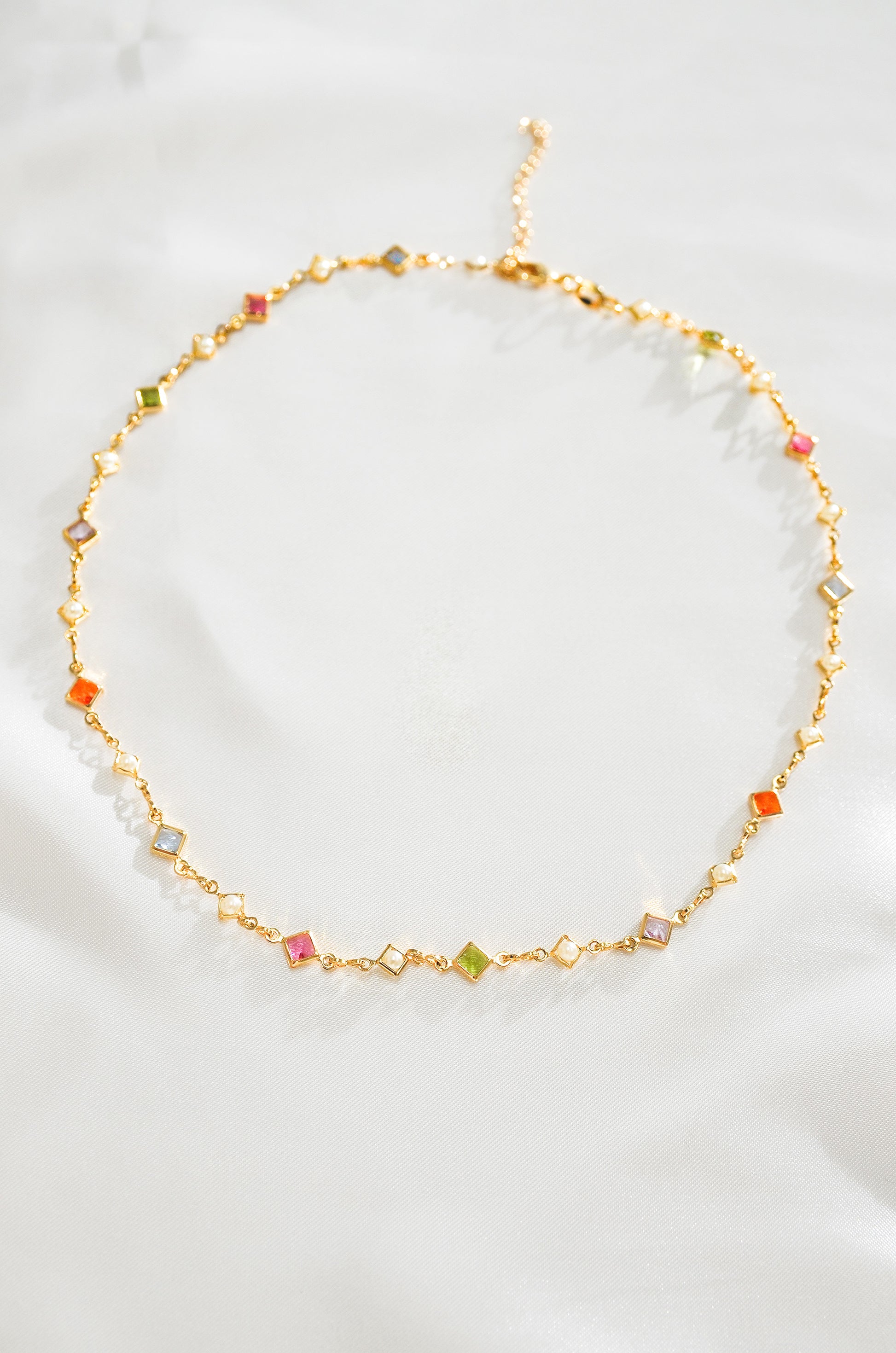 A gold-colored necklace with a series of multicolored crystal beads arranged in a chain link pattern.