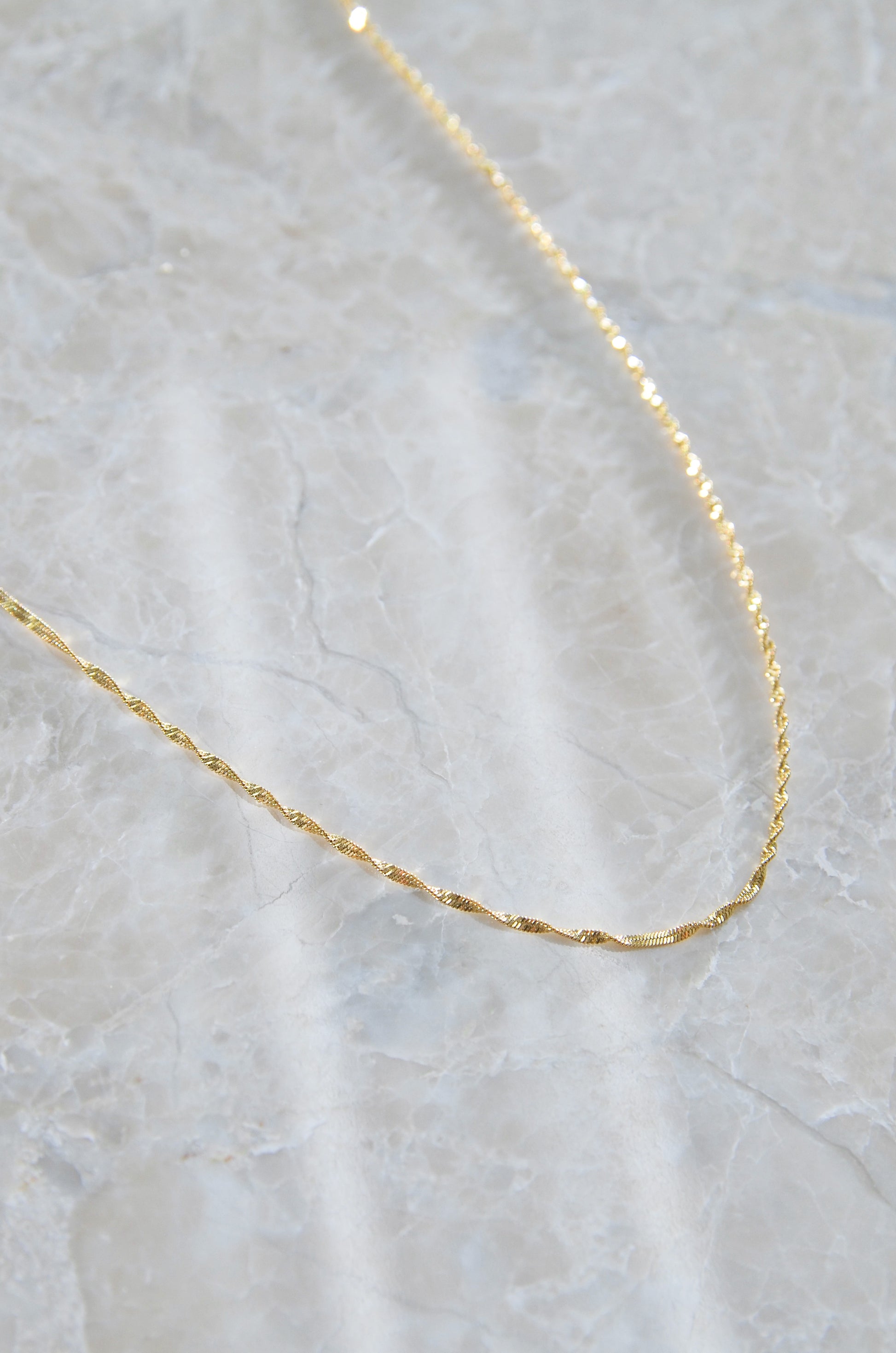 An 18K Gold Plated Manila Chain Necklace on a textured background, it's Waterproof & Non Tarnish. By DBL Jewelry
