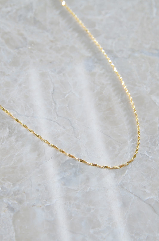 An 18K Gold Plated Manila Chain Necklace on a textured background, it's Waterproof & Non Tarnish. By DBL Jewelry
