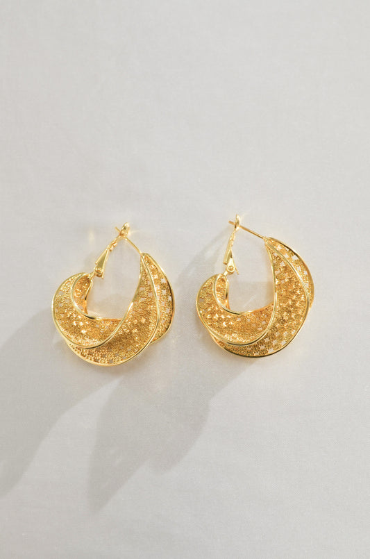 A pair of gold hoop earrings with intricate woven pattern detailing, placed against a white background.