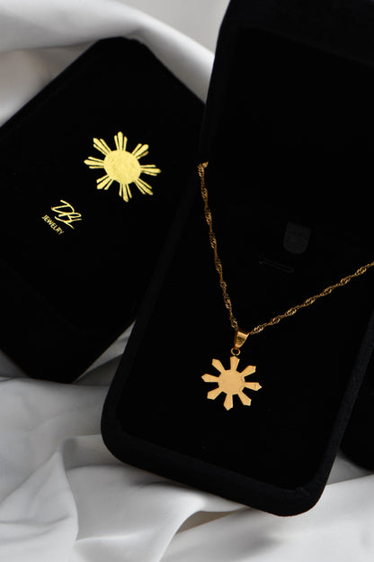 Black jewelry box with gold sun pendant necklace on a white fabric background